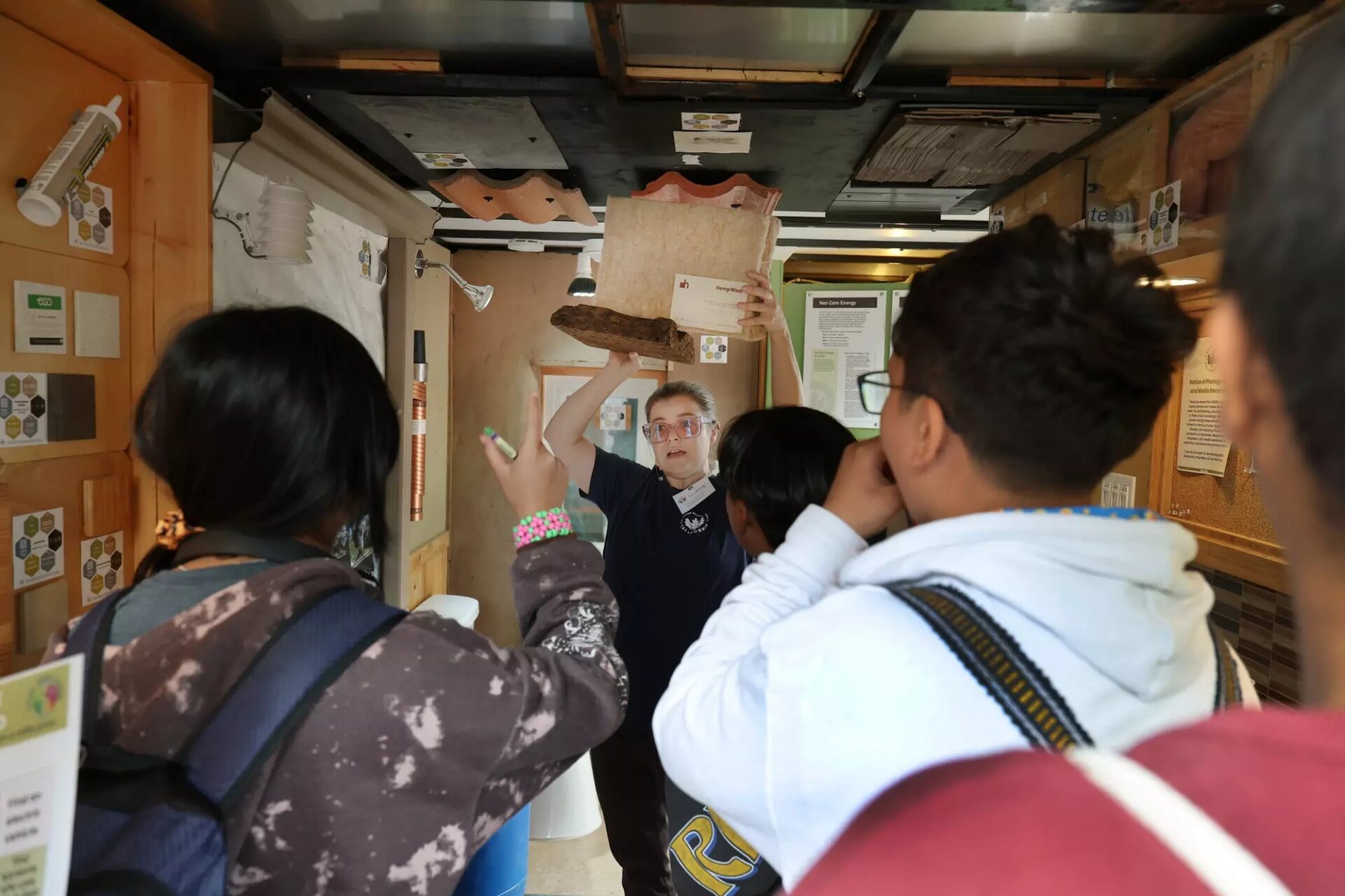 Instructor demonstrating roofing materials to a small group inside a training space, holding up samples while participants observe and ask questions.