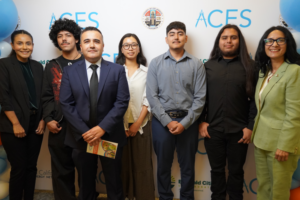 Six people, three men and three women of varying ages, stand smiling in a row against a white backdrop with 'ACES' logos and the County of Los Angeles seal. They are dressed in business casual and professional attire, indicating a formal event or program.