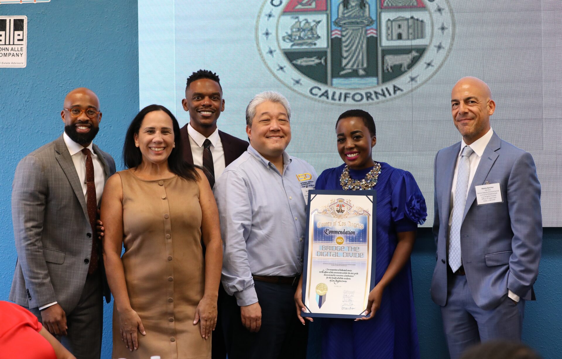 Six people smiling, holding a 'County of Los Angeles Commendation' certificate for 'Bridge the Digital Divide' in front of the county seal.